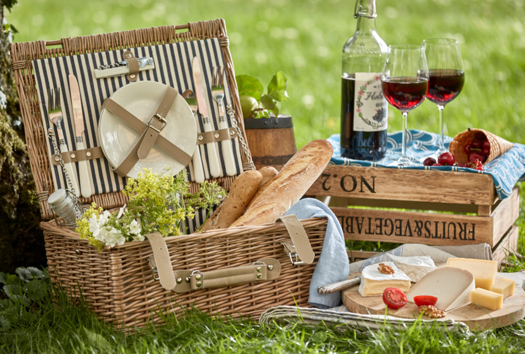 visit2go, Guided Tours Switzerland, Vintage style romantic summer picnic for two on lush green grass with a wicker hamper, French baguettes, assorted cheeses and red wine in stylish glasses